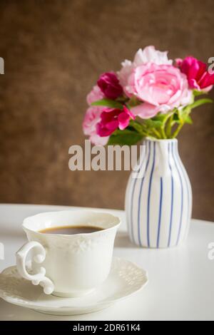 A cup of hot tea on the table behind it a stylish jug with a bouquet of flowers Stock Photo