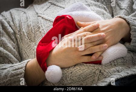 man in a christmas sweater, holding a santa hat and resting on the couch Stock Photo
