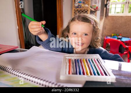 Happy young girl using children's colouring pens to draw on blank paper at home Stock Photo