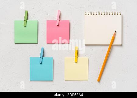 Four colorful blank adhesive notes notes every with wooden clothespin and spring notepad with pensil on a white concrete background. Plan tasks, share Stock Photo