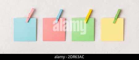 Four colorful blank adhesive notes every with wooden clothespin on a white concrete texture background. Plan tasks, share ideas, creativity concept. Stock Photo