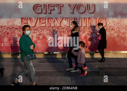 Pedestrians wearing face masks walk past a large size Christmas theme banner at the entrance of a shopping mall in Hong Kong.Hong Kong is currently experiencing a four wave of COVID-19 cases while the government has implemented new social restrictions and rules in the city. Stock Photo