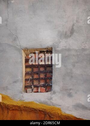 An old white and yellow painted wall and a bricked-up window with rusted bars. Stock Photo