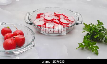 Fresh sliced radish with fresh green parsley close up on glass plate on light grey background. Woman serving vegetable salad Stock Photo