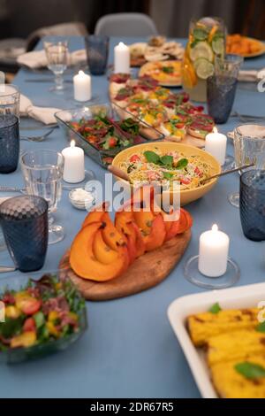 Festive table served with wineglasses, burning candles, vegetable salad, homemade sandwiches, pasta, baked pumpkin slices and grilled corn Stock Photo