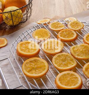 Making candied orange slices. Drying orange slices that have been cooked in syrup, on a rack un top of parchment paper and a basket of citrus fruit. Stock Photo