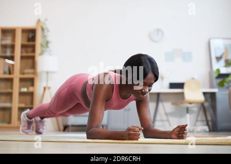 Full length portrait of young African-American woman doing plank exercise while enjoying workout at home, copy space above Stock Photo