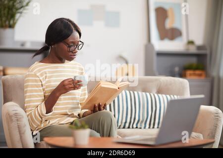 Portrait of young African-American woman reading in cozy home interior, copy space Stock Photo