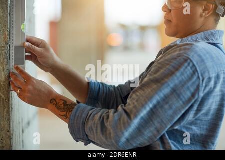 Cropped side view of female worker measuring wall level while working on construction site, copy space Stock Photo