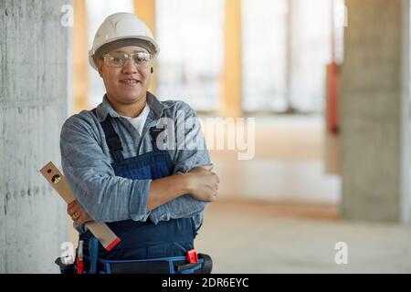 Waist up portrait of smiling female worker wearing hardhat and looking at camera while standing with arms crossed on construction site, copy space Stock Photo