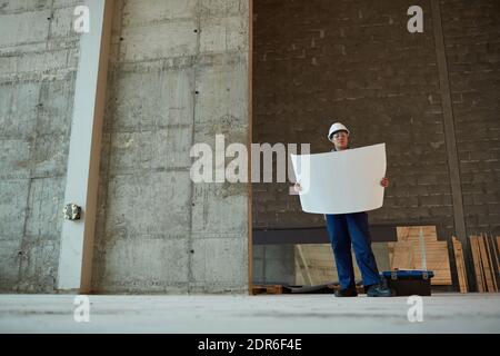 Wide angle view of female construction worker holding plans while working in apartment building, copy space Stock Photo