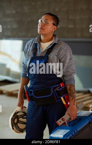 Vertical portrait of modern female worker holding toolbox while standing on construction site Stock Photo