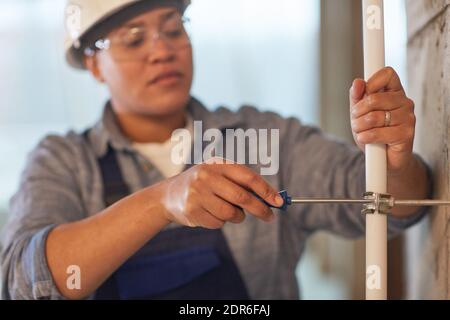 Close up of female worker setting up pipes while working on construction site, focus on foreground, copy space Stock Photo