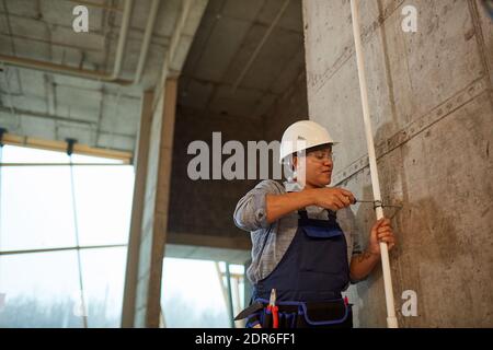 Wide angle portrait of female worker wearing hardhat and setting up pipes while working on construction site, copy space Stock Photo