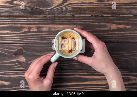 Female hands holding a cup of coffee with foam over a wooden table. with chocolate sprinkles Stock Photo