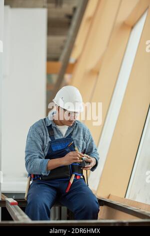 Vertical portrait of modern female construction worker wearing hardhat and holding tape measure while building metal frame on construction site Stock Photo