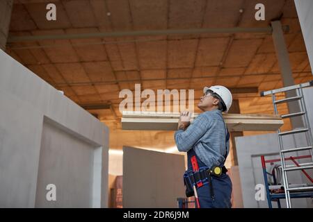 Side view portrait of modern female worker carrying wood boards while working on construction site, copy space Stock Photo