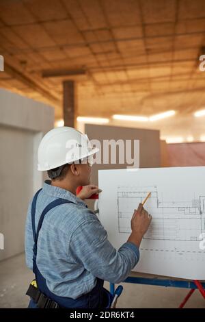 Vertical back view portrait of female engineer inspecting plans while working on construction site Stock Photo