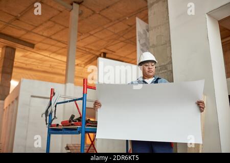Portrait of mature female worker holding blueprints while standing on construction site, copy space Stock Photo
