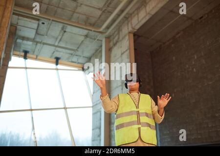Wide angle portrait of female engineer wearing VR headset on site while visualizing construction project, copy space Stock Photo