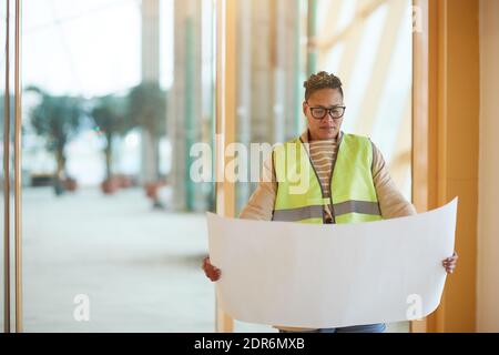 Waist up portrait of contemporary female engineer looking at blueprints while designing architectural project, copy space Stock Photo