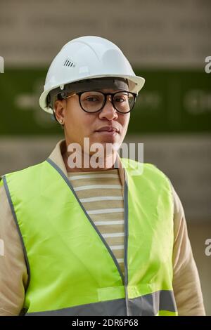 Vertical waist up portrait of modern female worker wearing hardhat and reflective vest while looking at camera on construction site Stock Photo