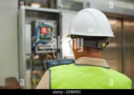 Back view at female worker wearing hardhat while inspecting electrical switchboard hub, copy space Stock Photo