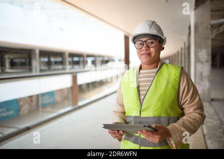 Waist up portrait of mixed-race female engineer holding digital tablet and smiling at camera while enjoying work on construction site, copy space Stock Photo