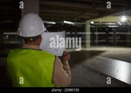 Back view at female engineer holding blueprints while inspecting base of building at construction site, copy space Stock Photo