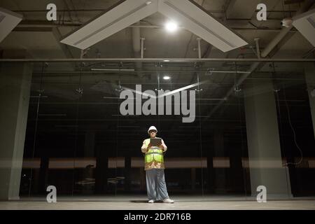Wide angle portrait of female engineer holding digital tablet while inspecting base of building at construction site, light and shadow, copy space Stock Photo