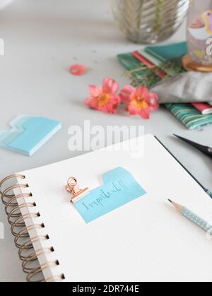 Empty spiral notebook with a dotted pencil and an important note clamped at the top of it. A stack of blue notes are next to it. Stock Photo