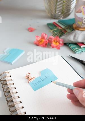 Empty spiral notebook with a dotted pencil held by a woman hand and an important note clamped at the top of it. Stock Photo