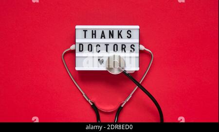 Text board for with text thank you doctors,stethoscope on red background,top view,flat lay.Thanks to doctors,nurses and all medical personnel working Stock Photo