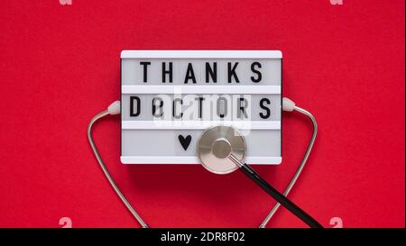 Text board for with text thank you doctors,stethoscope on red background,top view,flat lay.Thanks to doctors,nurses and all medical personnel working Stock Photo