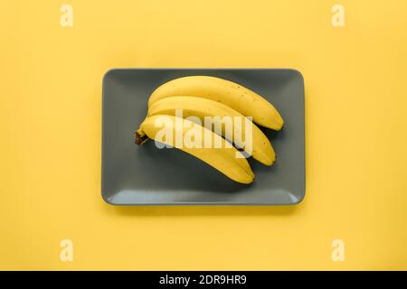 Bananas on a gray plate on a yellow background. Top view, flat lay. Stock Photo