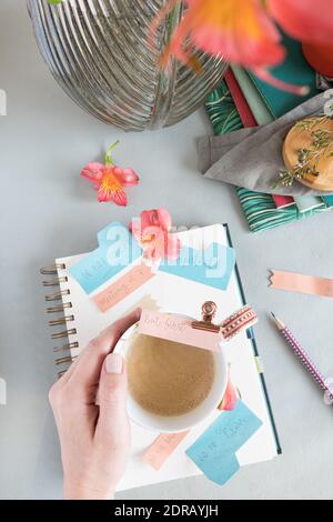 Woman hand holding a foamy coffee over a spiral notebook full of multicolor reminder notes on a clean background. Stock Photo