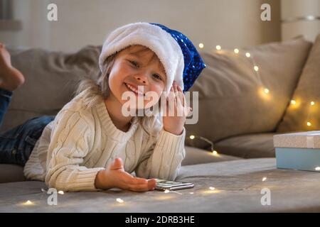 Portrait of girl in blue Santa hat using mobile phone for video call friends and grandparents. Stock Photo