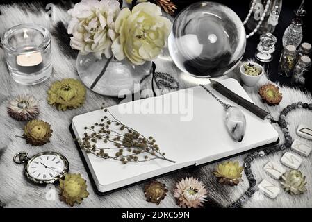 Styled still life with open book diary with copy space, crystal ball, runes, yellow flowers and ritual magic object on witch table. Esoteric, gothic a Stock Photo
