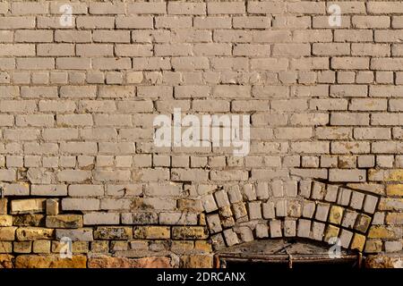 Full frame view of an eroding antique exterior brick wall surface with white painted bricks and an arched basement window covered with a rusty grate. Stock Photo