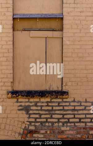 Texture background of a rugged old exterior beige painted exterior brick wall with a boarded up old window and stained eroding brickwork Stock Photo