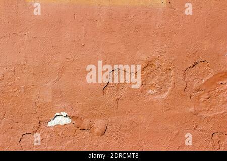 Full frame abstract background of an eroding exterior concrete stone wall with cracked and peeling red painted stucco plaster surface texture Stock Photo
