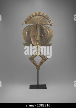 Reliquary Figure, 19th century, Wood, brass, copper, iron, and cowrie shells, 28 1/8 × 14 3/4 × 2 3/8 in. (71.5 × 37.5 × 6 cm), Kota reliquaries emphasize the head. From this stylized, flattened rendering of the human head with a popular nineteenth-century men’s coiffure extends a lozenge representing an abstraction of the upper body. A basket or bundle containing ancestral remains was attached to this schematic representation of the body. Several such reliquaries were housed in a community enclosure for the unity of local ancestors Stock Photo