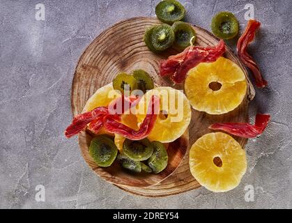 Dried fruits: Yellow candied pineapple rings, red papaya and green kiwi on a wooden board Stock Photo