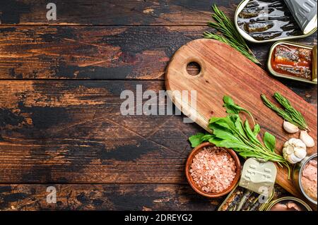 Opened cans conserve with saury, salmon, sprats, sardines, squid and tuna. Dark Wooden background. Top view. Copy space. Stock Photo