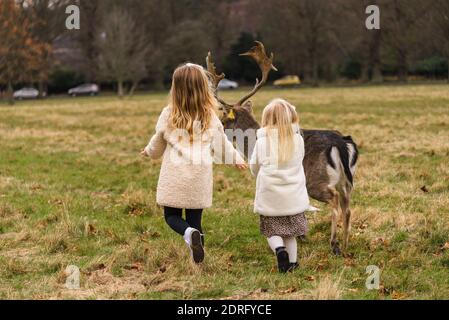 Two cute blonde girls running near friendly deer at the Phoenix Park in Dublin, Ireland Stock Photo