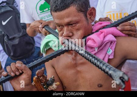 During the Vegetarian Festival in Phuket Town, Thailand, a Mah Song or spirit medium sits with cheeks pierced by massive iron rods Stock Photo