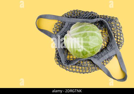 A head of cabbage lies in an ecological string bag on a yellow background. Eco friendly shopping, environmental protection concept. Colors of the Year Stock Photo