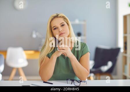Supportive good-looking woman sitting at desk, attentively listening and looking at camera Stock Photo