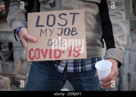 Engineer stands with plastic cup and holds placard Lost my job due covid-19 Stock Photo
