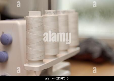 Detail of four thread spools with white thread on overlock sewing machine Stock Photo